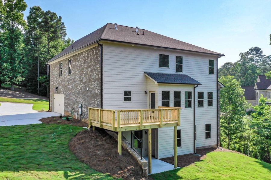 Back view of a two-story house with a wooden deck, brick and siding, on a sunny day.
