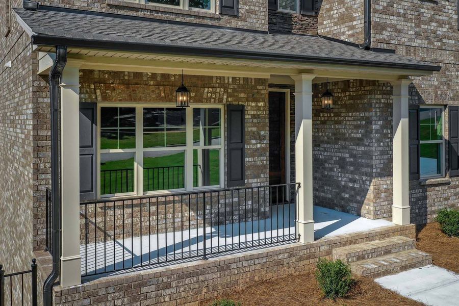 Brick home porch with white columns, black railing, and two steps.