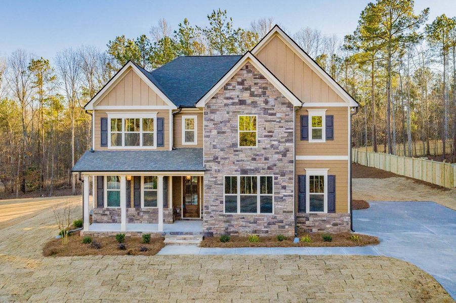 Two-story house with stone facade, brown siding, blue shutters, and a driveway, set in a wooded area.