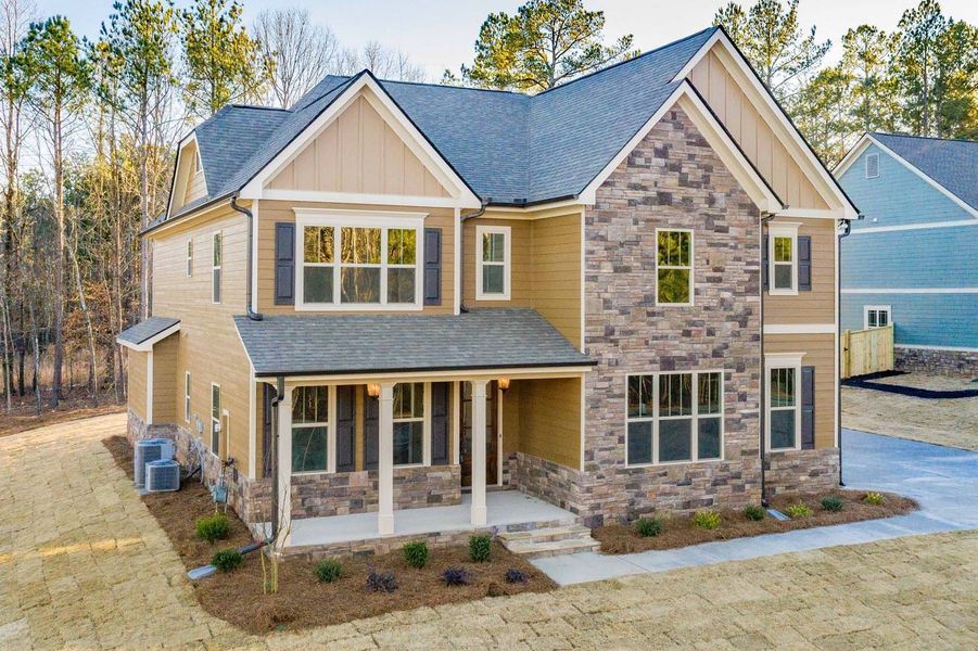 Two-story house with tan siding, stone facade, gray roof, and covered porch.