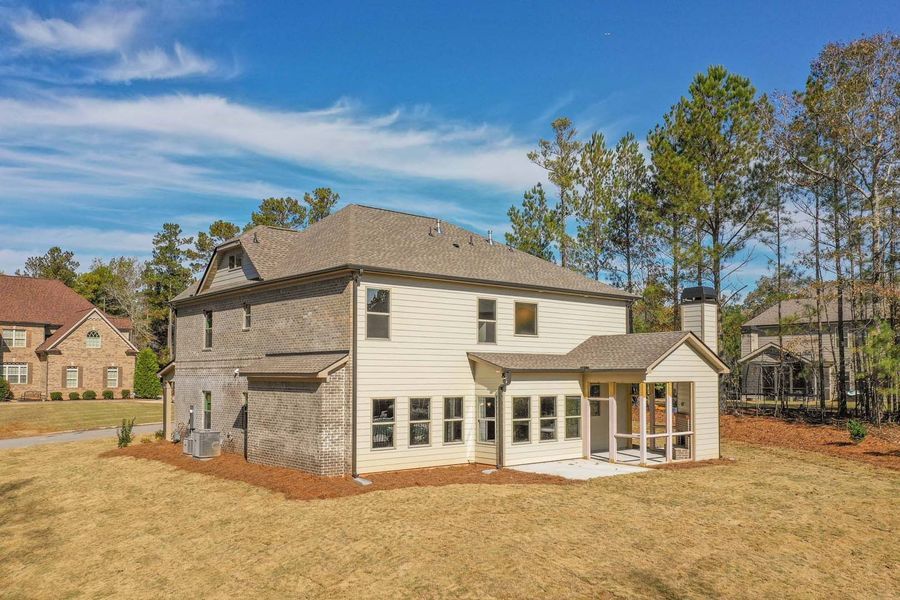 Back view of a two-story house with light siding, brick, and a porch under a blue sky.