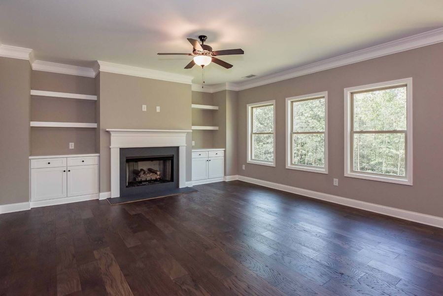 Empty living room with fireplace, built-in shelves, and dark wood floors. Beige walls, white trim.