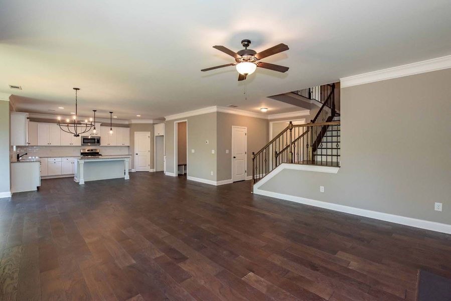 Open-concept living space with kitchen, hardwood floors, neutral walls, and staircase.