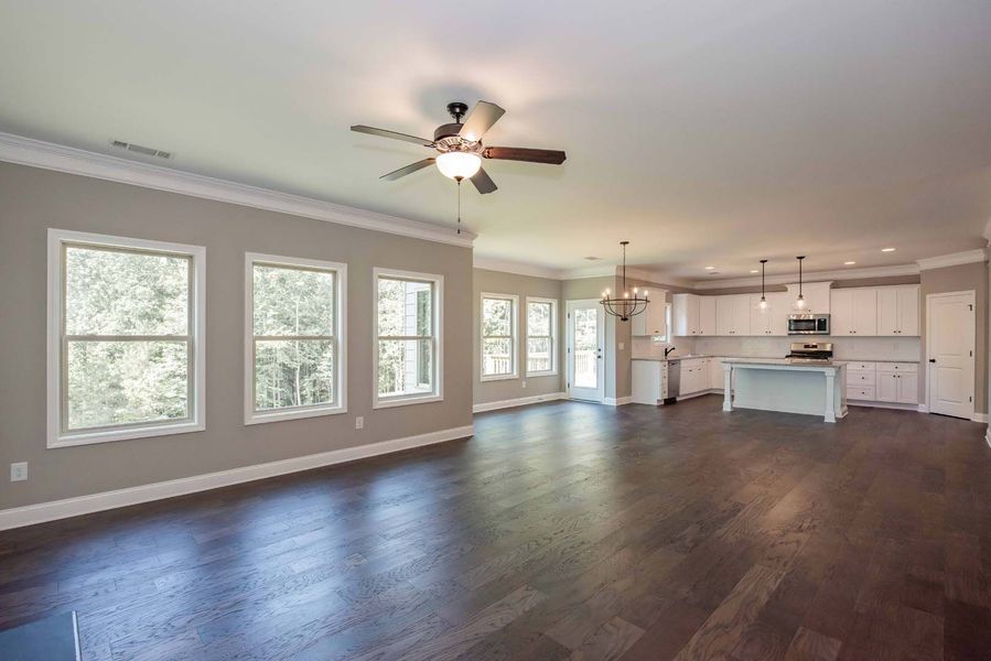 Spacious, empty living space with dark wood floors, white kitchen, and large windows.