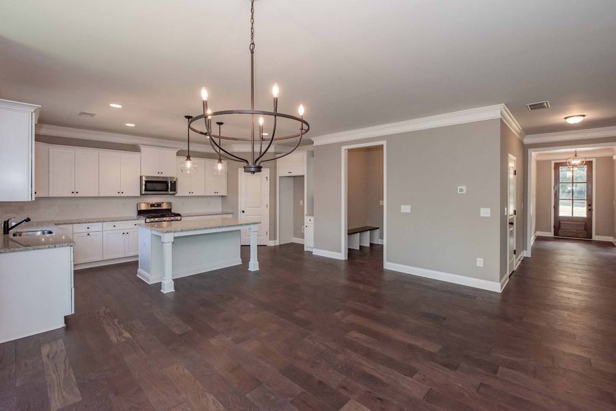Open-concept kitchen with white cabinets, island, and a chandelier; dark wood floors and neutral walls.