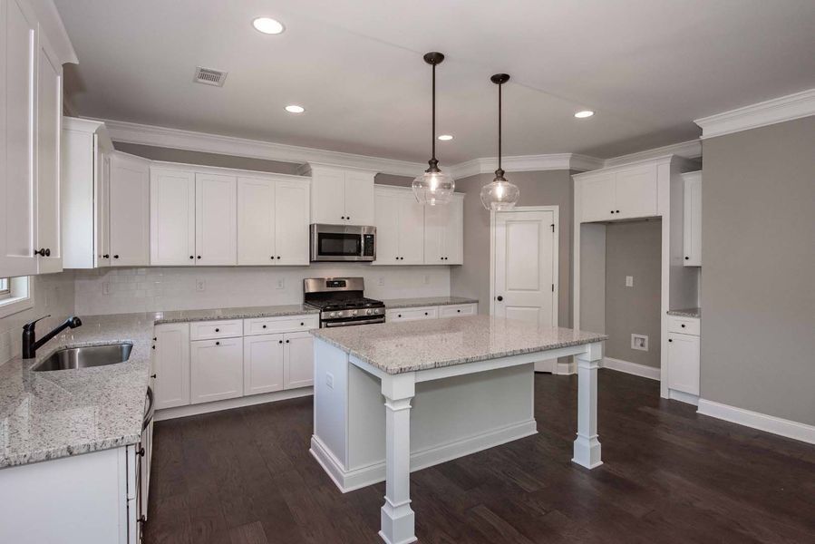 Bright white kitchen with island, granite countertops, and dark wood floor.