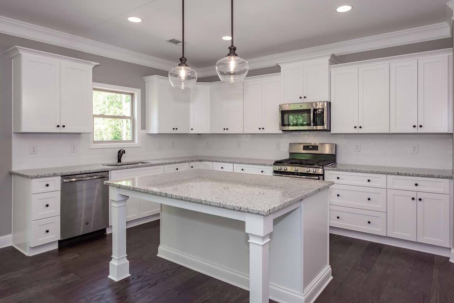 White kitchen with gray countertops, stainless steel appliances, and dark wood floors.