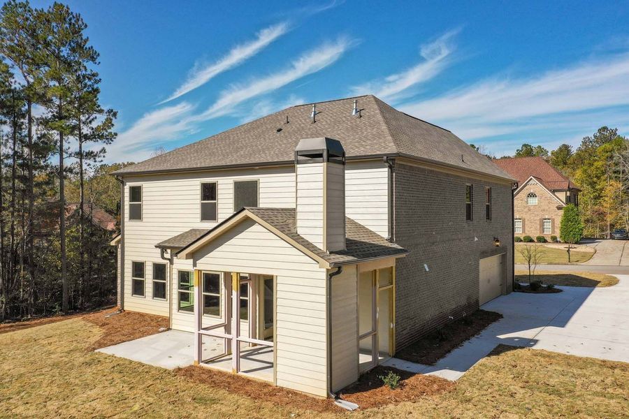 Back view of a two-story beige house with a screened porch and chimney on a sunny day.