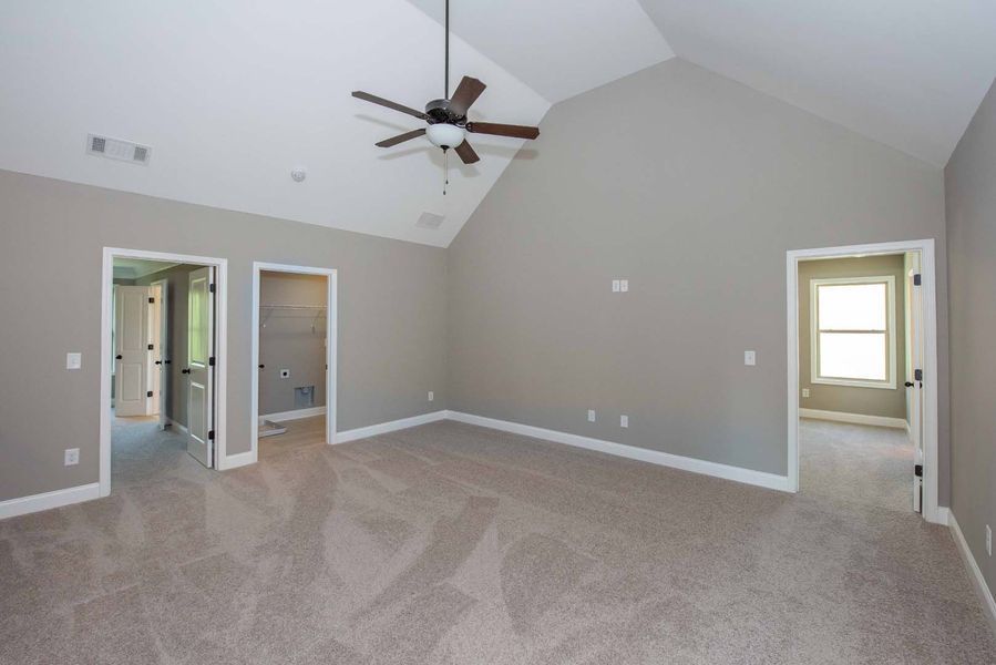Spacious bedroom with gray walls, carpet, and a ceiling fan, with doorways to other rooms.
