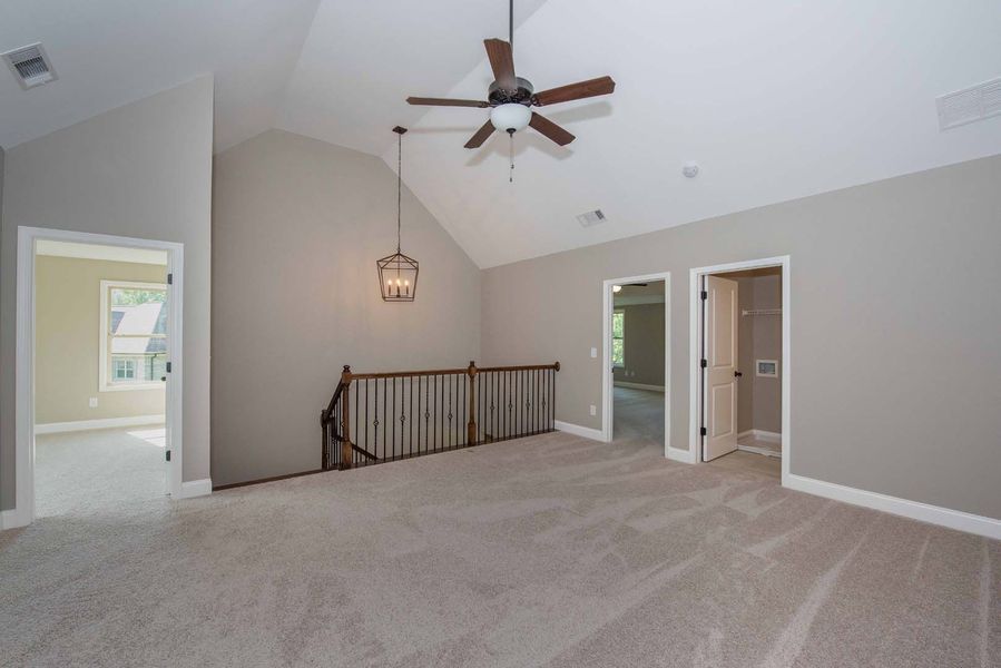 A carpeted loft with neutral walls, a staircase, a ceiling fan, and multiple doorways.