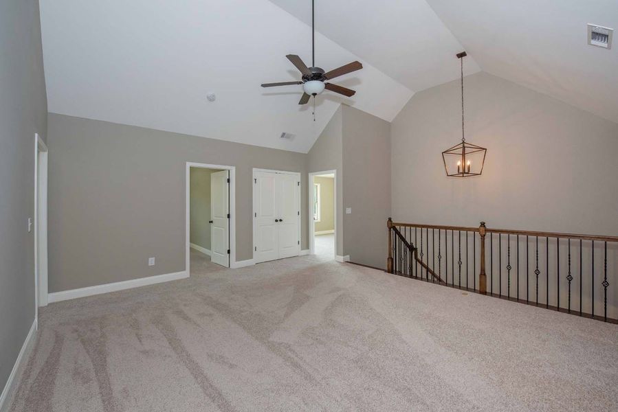 Spacious room with vaulted ceiling, neutral walls, carpet. Includes ceiling fan, chandelier, doors, and staircase.