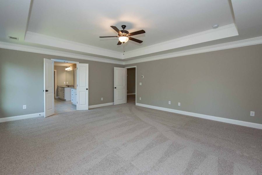 Empty bedroom with beige carpet, gray walls, and white trim, two doors open to a bathroom.