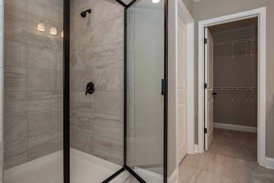 Bathroom with a gray tiled shower, black framed glass door, and a closet with wire shelving.