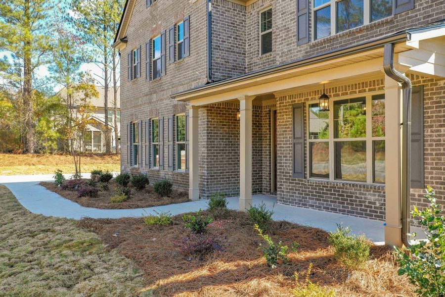Brick two-story house with a covered porch and manicured landscaping on a sunny day.