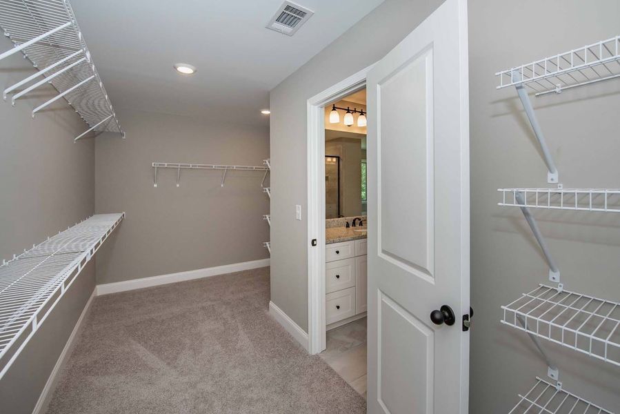 Walk-in closet with wire shelves and a door leading to a bathroom with a sink and mirror.