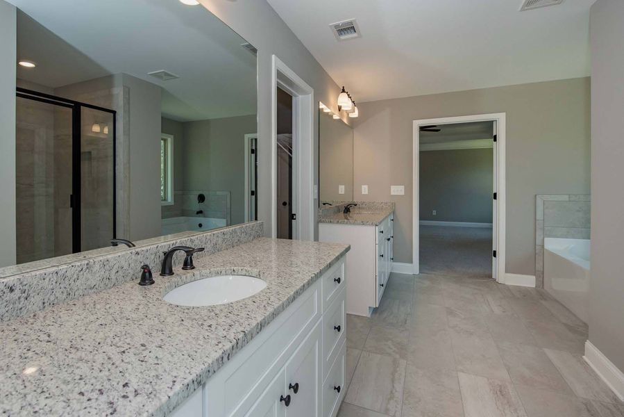 Spacious bathroom with white cabinets, granite countertop, large mirror, and grey tile flooring.