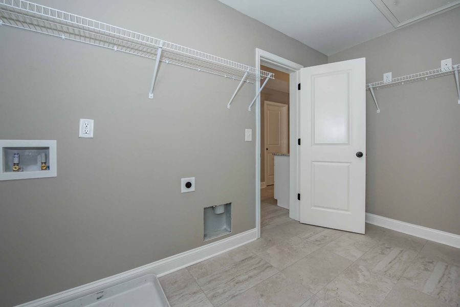 Empty laundry room with gray walls, white shelves, and a door to another room.