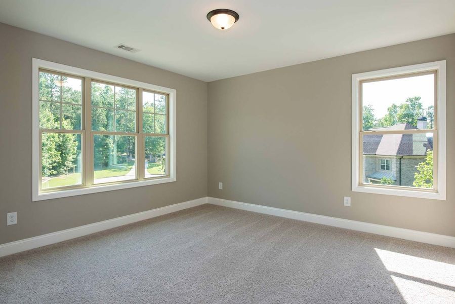 Empty bedroom with light gray walls, two windows, beige carpet.