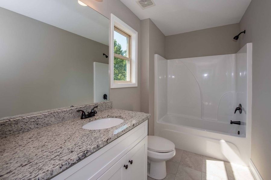 Bathroom with white cabinets, granite countertop, tub/shower, window.