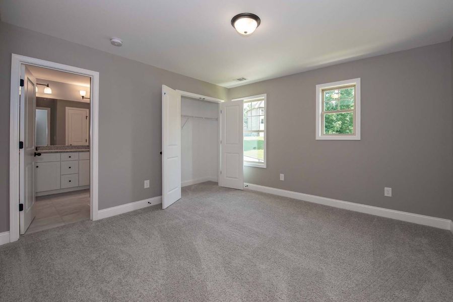 Gray bedroom with closet, bathroom doorway, window, and carpet.