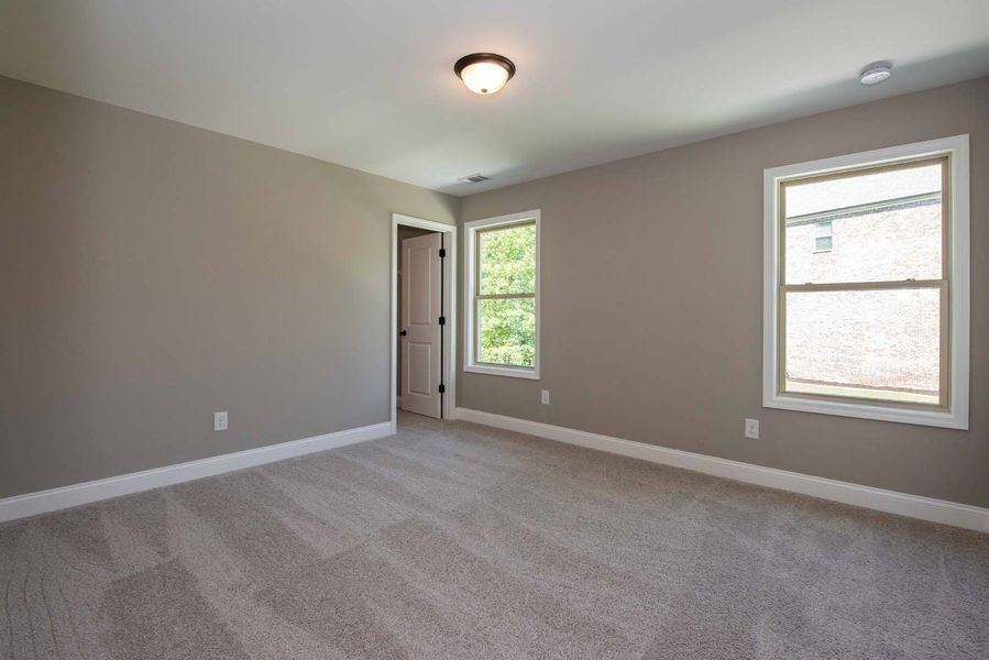 Empty bedroom with beige walls, carpet, two windows, and a door.