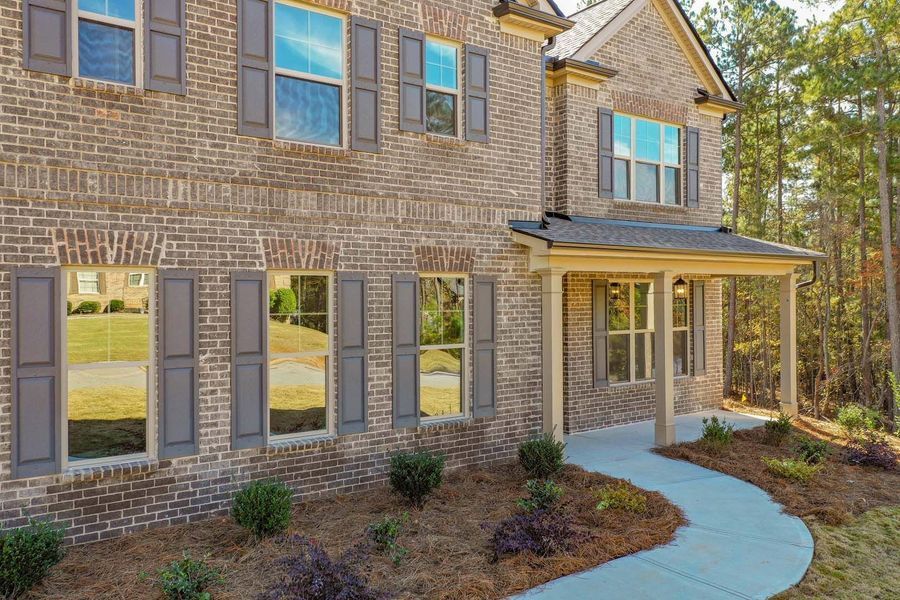 Brick house with gray shutters and a covered porch; a winding concrete walkway leads to the front door.