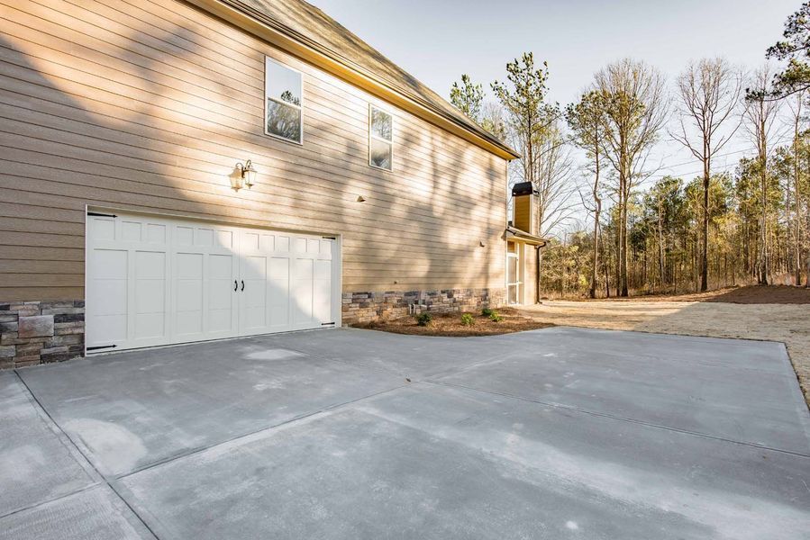 Garage with white door, attached to a beige house, with concrete driveway and trees in the background.