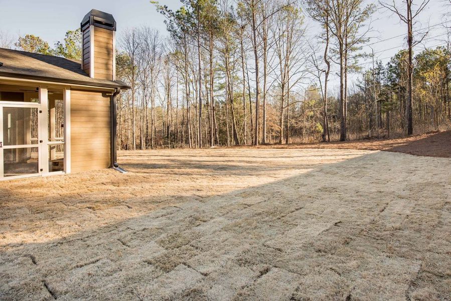A home's backyard featuring sod blocks leading to a grassy area, with trees in the background.
