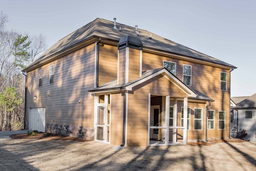 Rear view of a two-story house with a porch. Tan siding, brown roof. Sunny day.