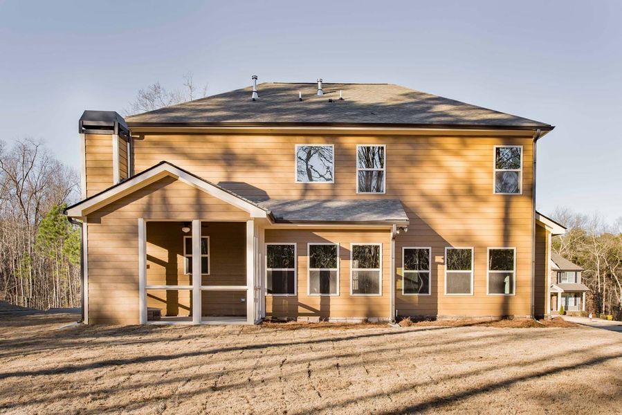 Back view of a two-story beige house with a porch and many windows, set on a grassy area.