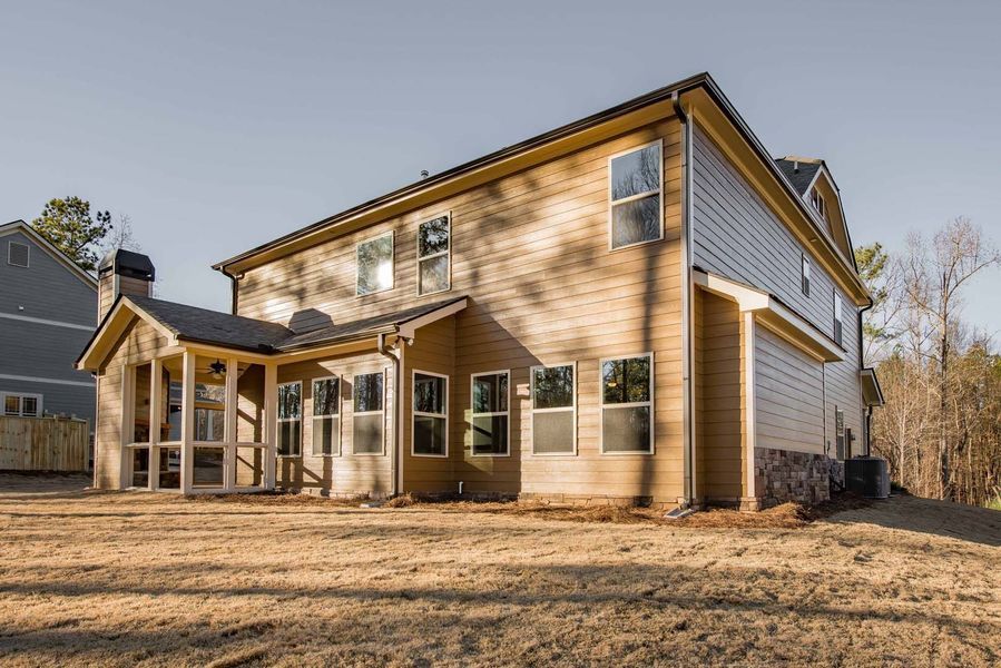 Two-story house with light brown siding and a screened porch in a grassy yard on a sunny day.