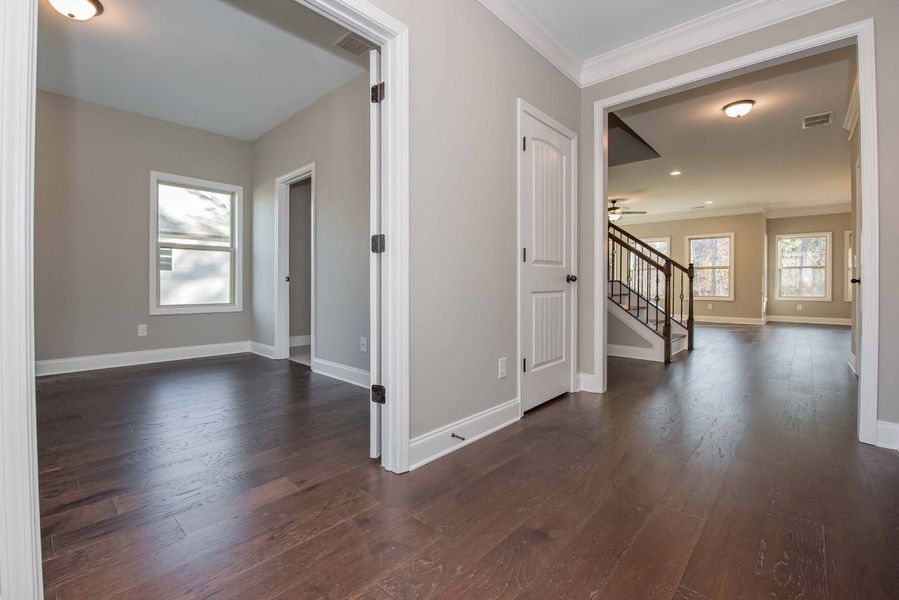 A hallway with dark wood floors, light gray walls, white trim, and doors leading to rooms.