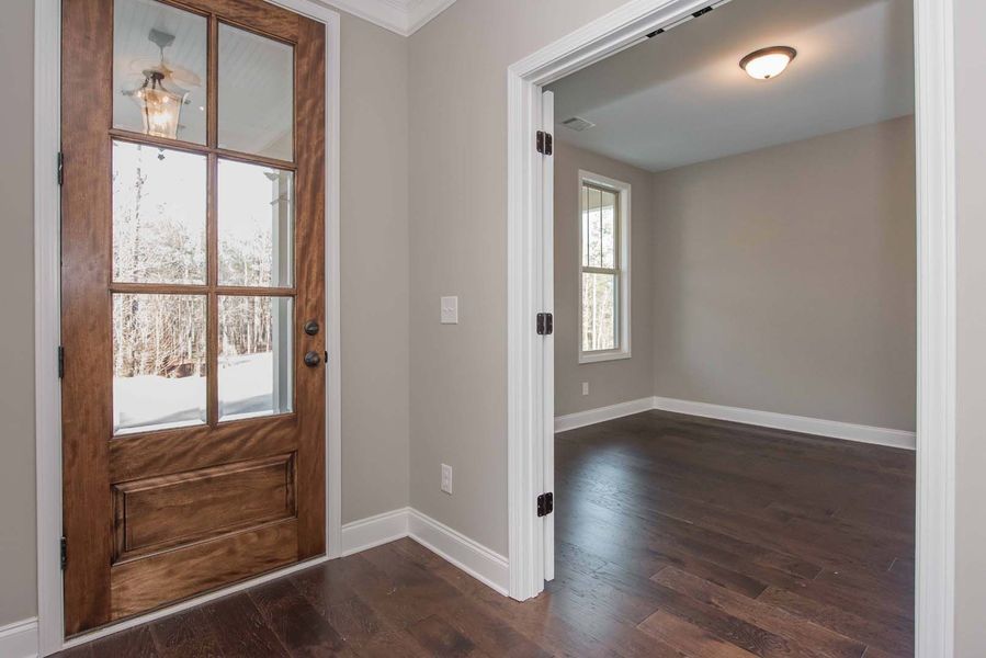 Wooden front door with glass panels, leading into a room with dark wood floors and neutral walls.