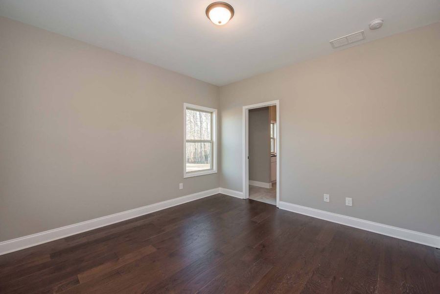 Empty bedroom with dark wood floor, gray walls, and white trim. Doorway and window visible.