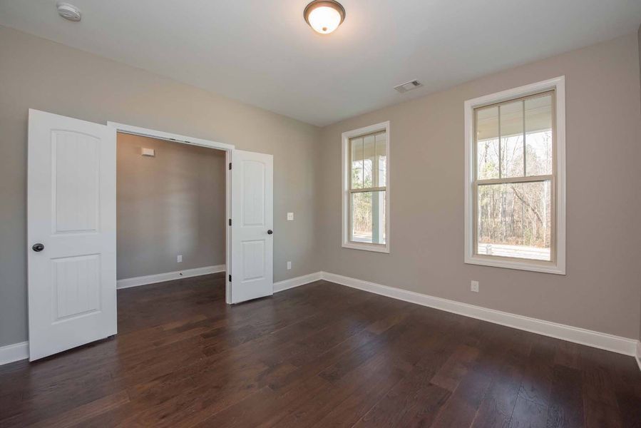 Empty bedroom with hardwood floor, two windows, and double doors, tan walls.