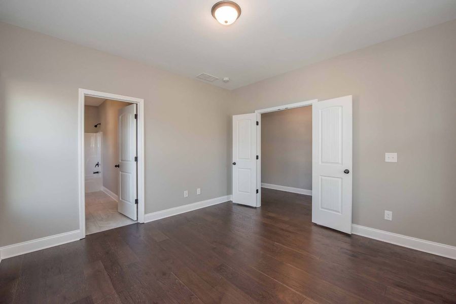 Empty room with dark wood floors, neutral walls, and three white doors.