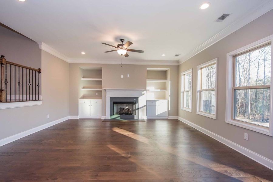 Spacious living room with fireplace, built-in shelves, dark wood floors, and large windows overlooking trees.
