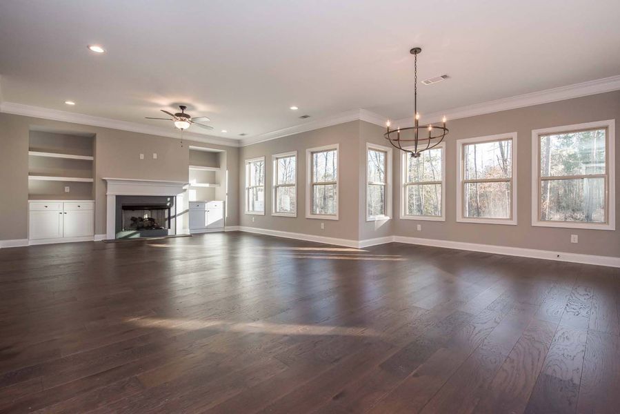 Spacious living room with hardwood floors, fireplace, built-in shelves, and multiple windows with natural light.