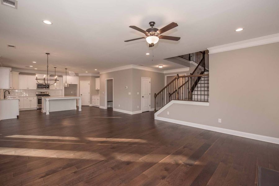 Spacious open-concept interior with hardwood floors, kitchen, staircase, and ceiling fan.