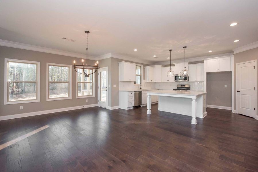 Open-concept kitchen and living area with white cabinets, an island, dark wood floors, and windows.