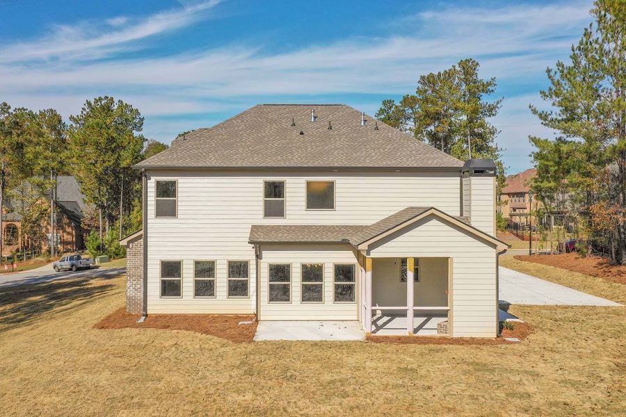 Back of a two-story white house with a porch. Trees and grass surround the house.