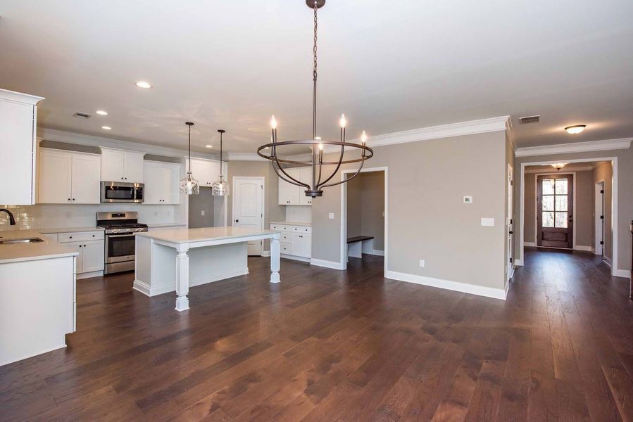 Spacious kitchen with white cabinets, island, dark wood floors, and chandelier.