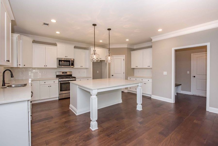 White kitchen with a large island, hardwood floors, and stainless steel appliances.