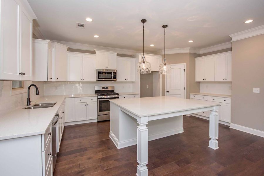 White kitchen with island, cabinets, and dark wood floors; two hanging lights above the island.