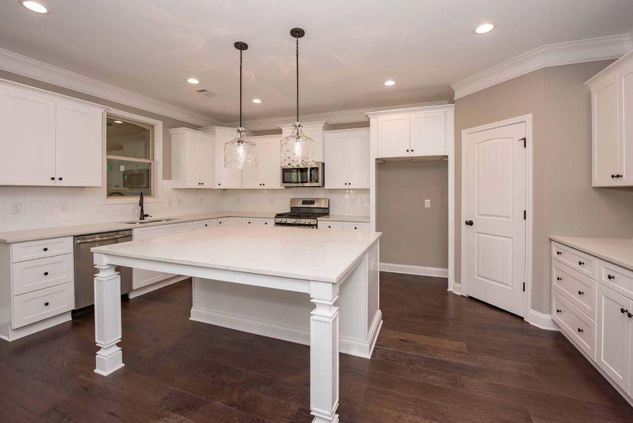 Bright white kitchen with island, cabinets, and dark wood floors. Two pendant lights hang over island.