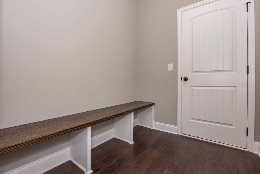 A built-in wood bench with white supports against a grey wall, next to a white door on hardwood floors.