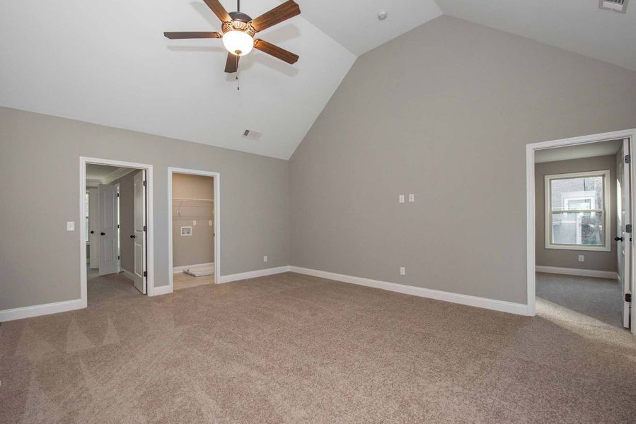 Spacious bedroom with vaulted ceiling, neutral walls, carpet, and three doorways.