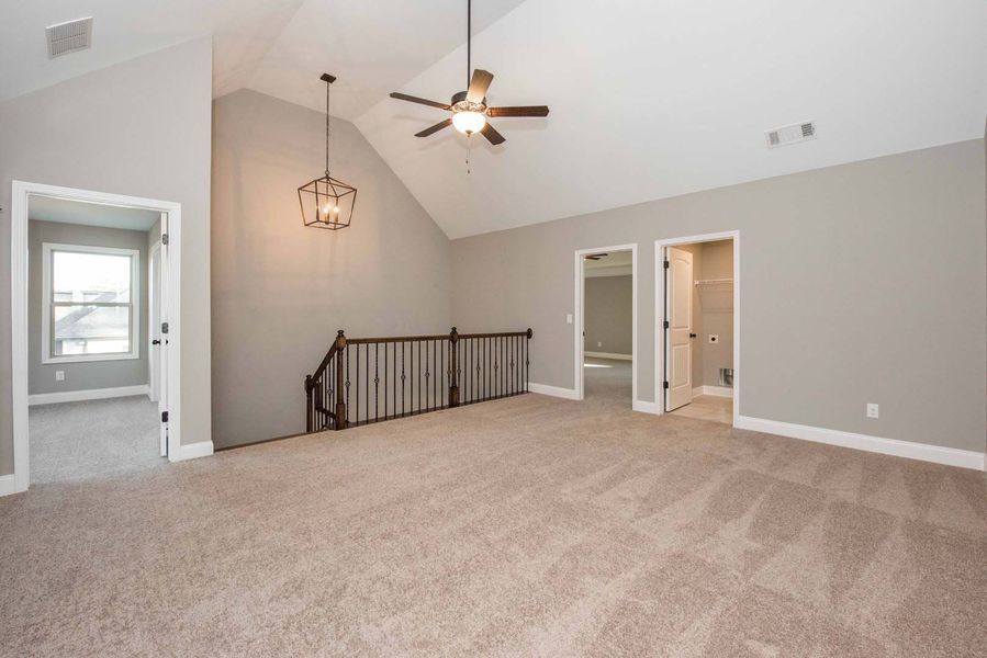Spacious room with vaulted ceiling, carpeted floors, staircase with railing, and two open doors.