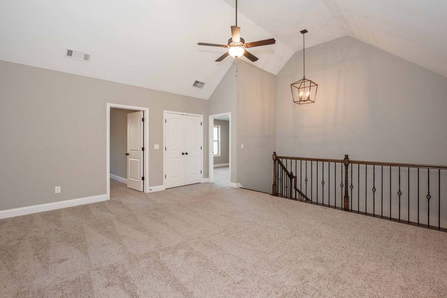 Spacious room with gray walls, carpet, a ceiling fan, chandelier, and a railing.