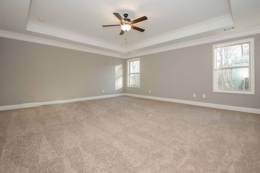 Empty bedroom with beige carpet, gray walls, and white trim; ceiling fan.